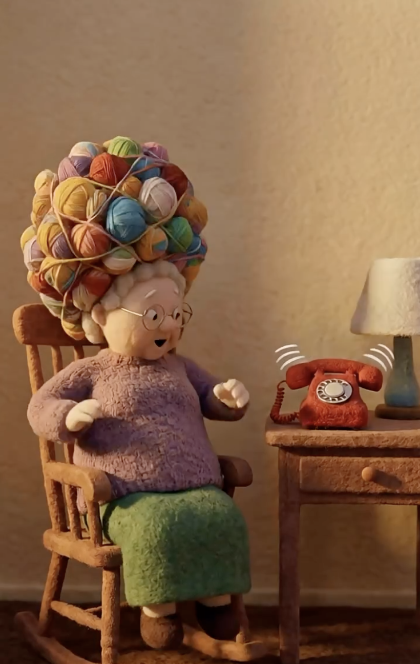 Vovó de feltro com cabelo de novelos de lã ao lado de um telefone vermelho
